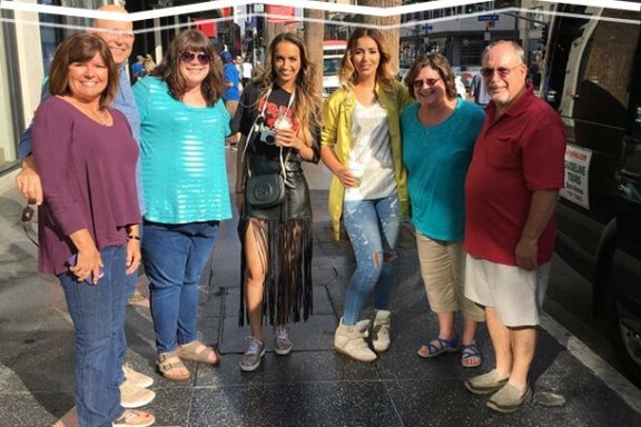 Group of seven people smiling on a city sidewalk with a star on the ground.