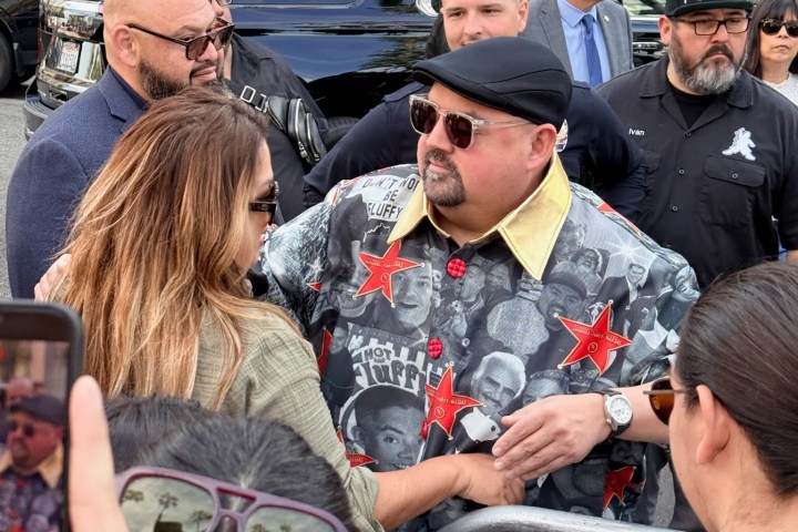 Man in star-patterned shirt greets fans near a barricade.