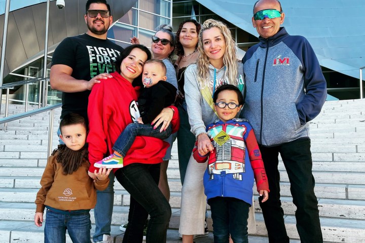 Group of adults and children smiling on outdoor steps with modern building background.