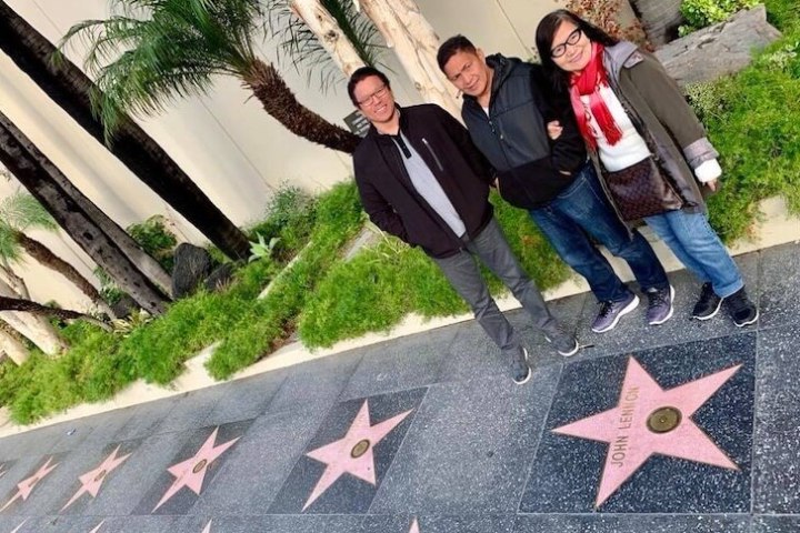 Three people standing near stars on a Hollywood Walk of Fame sidewalk.