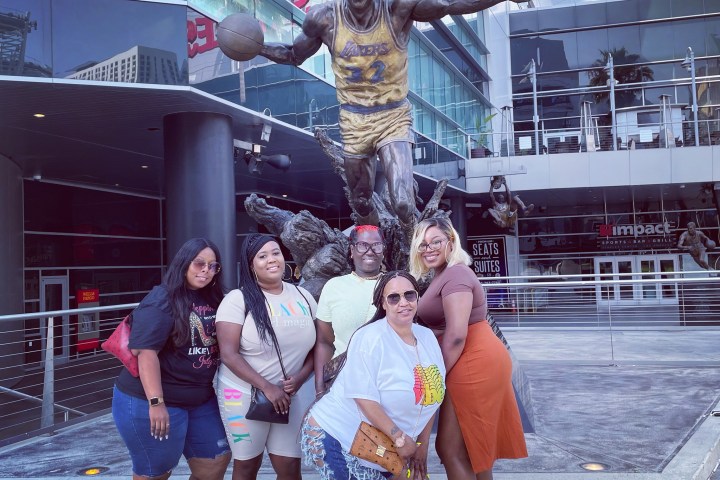 Group of five people posing in front of a basketball player statue.