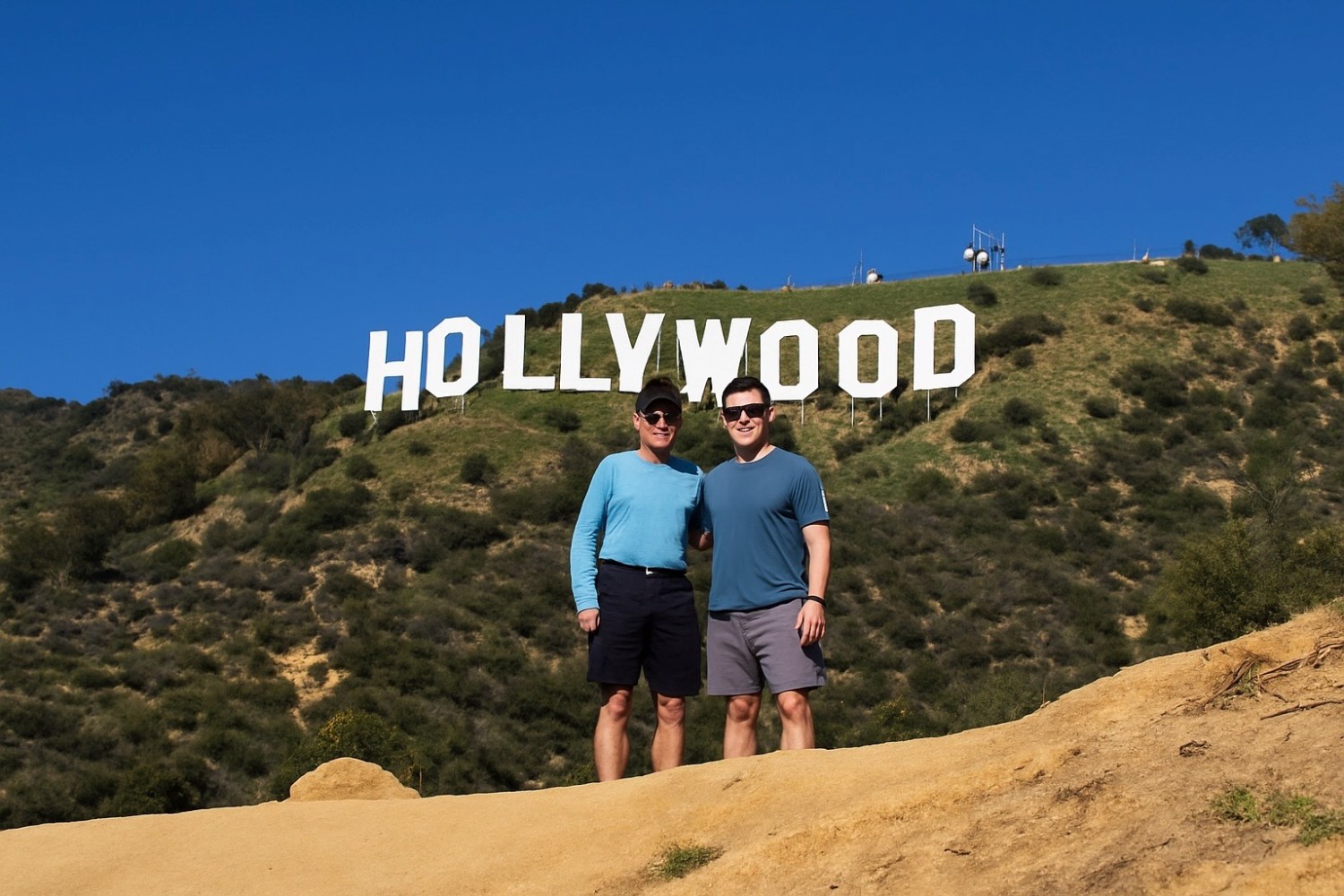 Father and son from Chicago posing together directly in front of the Hollywood Sign on the hiking trail viewpoint