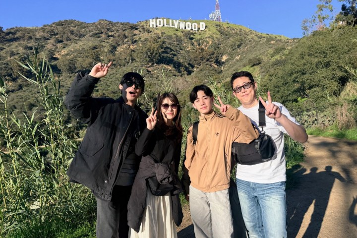 Four people posing on a trail with the Hollywood sign visible in the background.