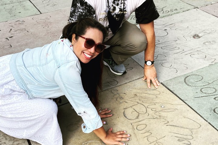 Two people posing by celebrity handprints on a sidewalk.