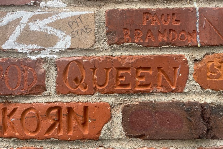 Brick wall with band names 'QUEEN' and 'KORN' engraved.