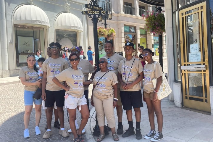 Group of nine people in matching shirts smiling on a city street corner.