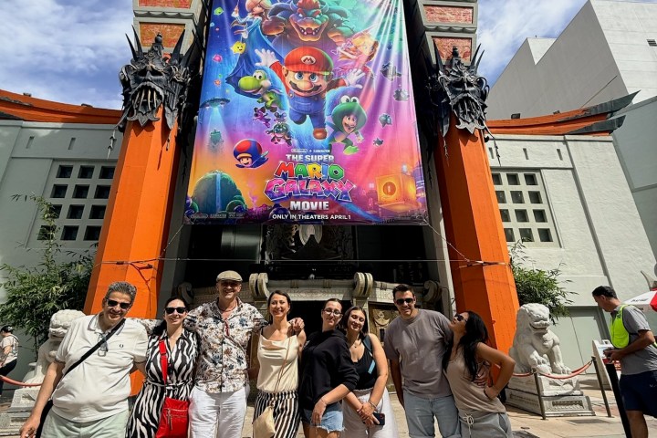 Group posing in front of a theater with a colorful movie poster.