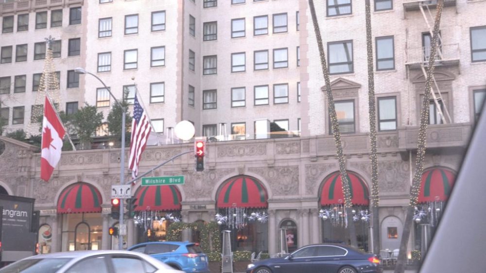 City street with flags, decorated building, red awnings, and passing cars.