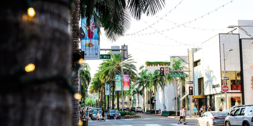 Street view with palm trees, buildings, and people walking.