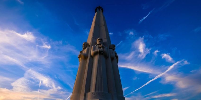 Tall monument with statues under a blue sky with clouds.