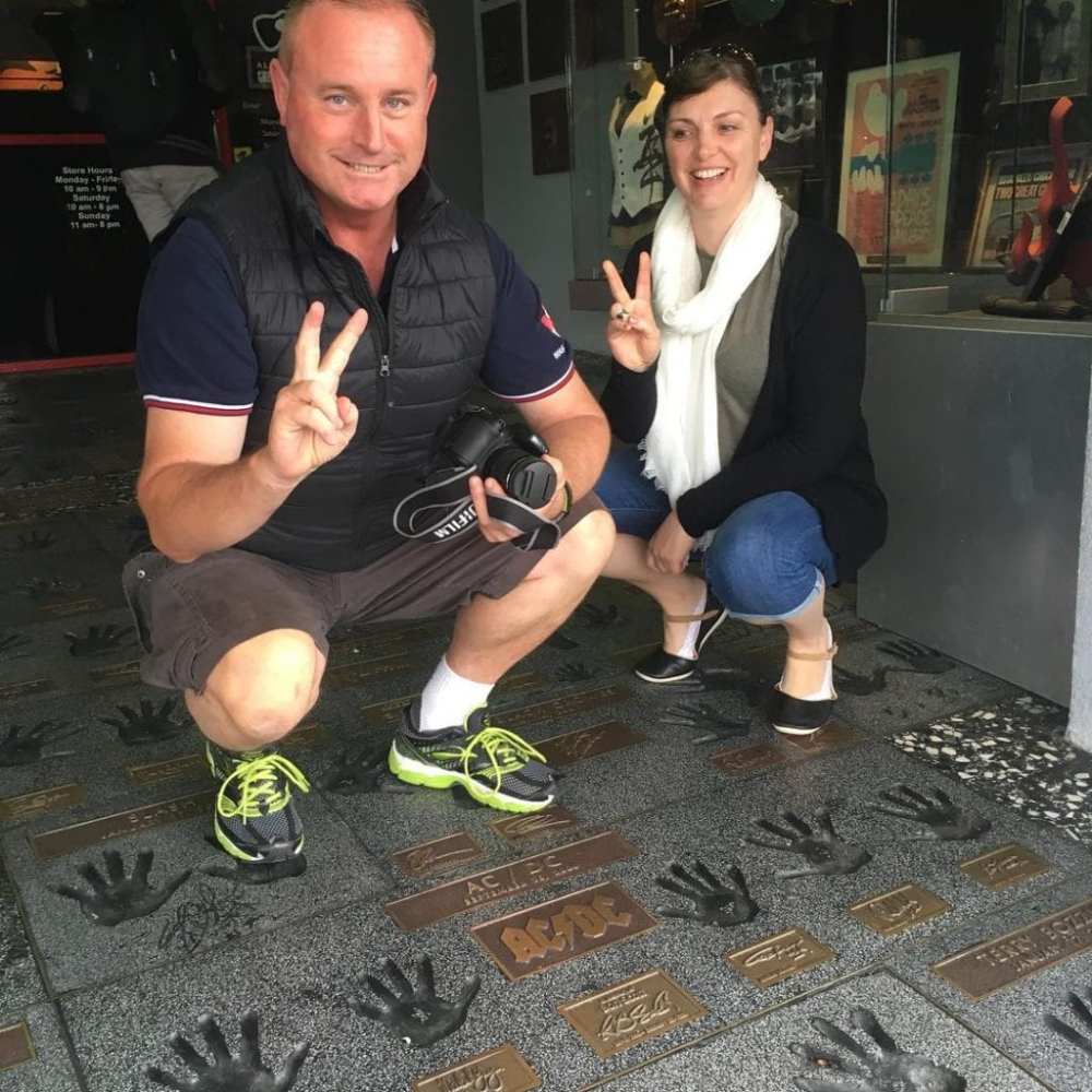 Two smiling people posing with peace signs on a handprint sidewalk.