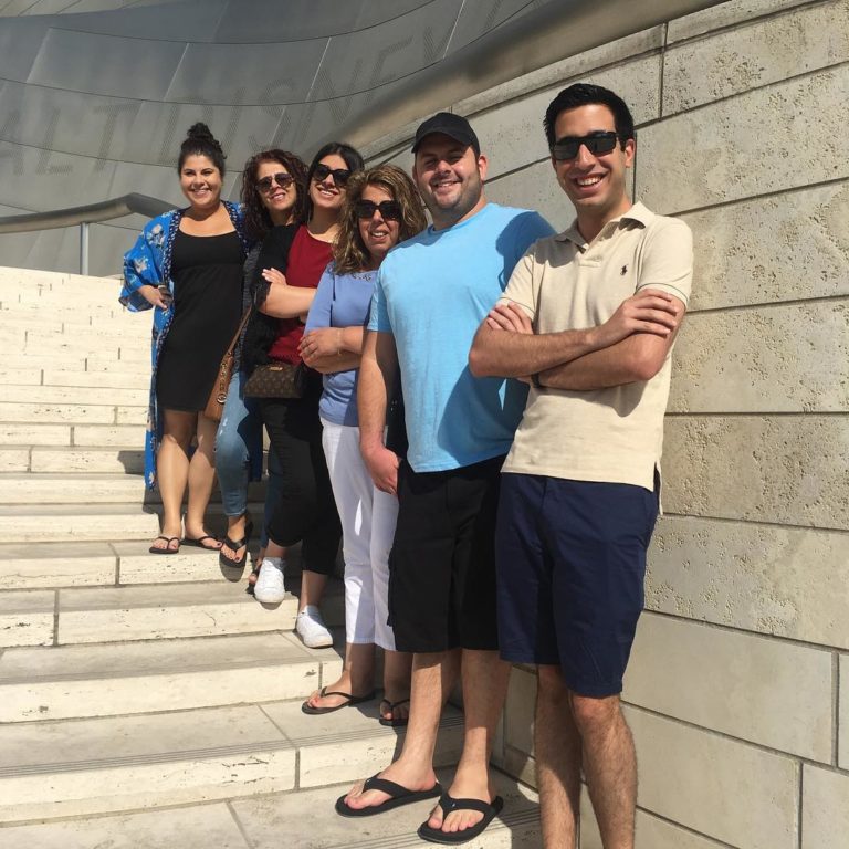 Group of six people smiling while standing on outdoor steps.