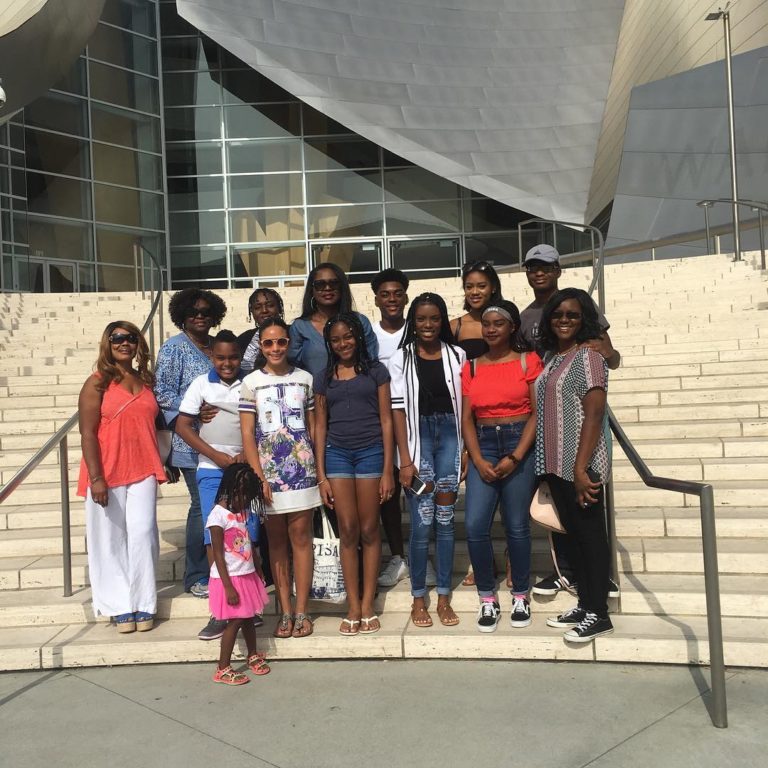 Group of people posing on steps in front of a modern building with curved metal facade.