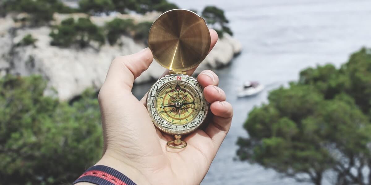 Hand holding a vintage compass near a scenic water view.