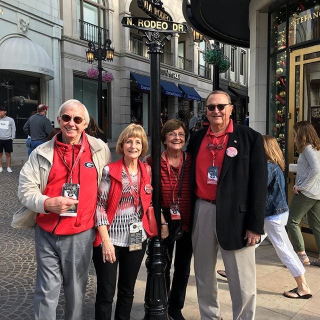 Group of four smiling adults in red attire standing by N. Rodeo Dr. sign