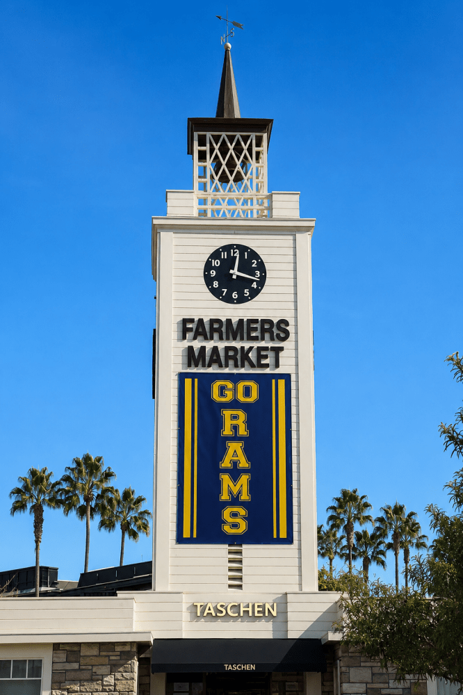Original Farmers Market clock tower in Los Angeles with blue sky, palm trees, and a Go Rams banner on the historic Farmers Market sign.