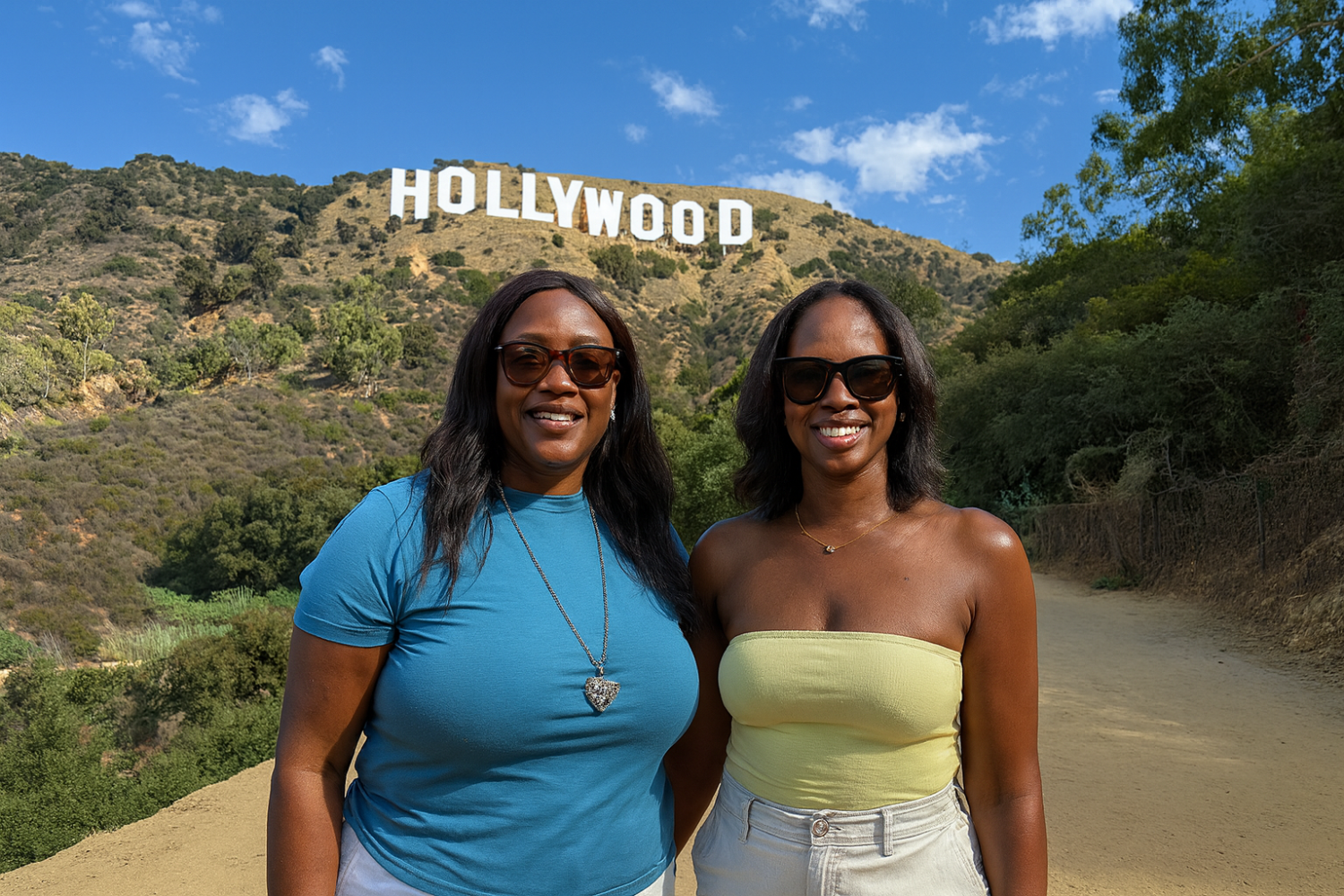 Two women from Nigeria smiling on the Hollywood Sign hiking trail with the iconic white letters visible on the hillside behind them