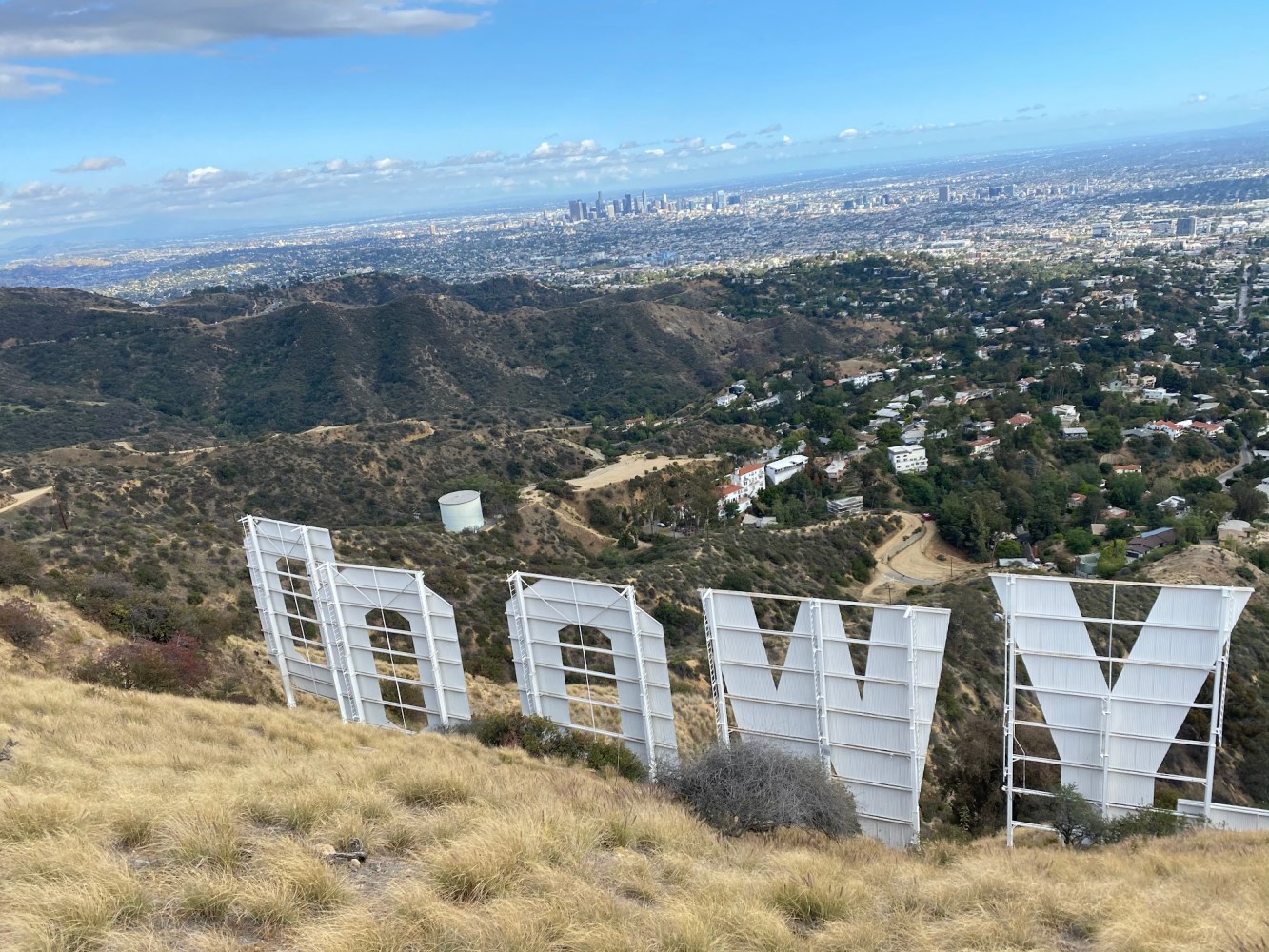 View from behind the Hollywood Sign showing the steel scaffolding structure of the letters with downtown Los Angeles skyline visible in the distance