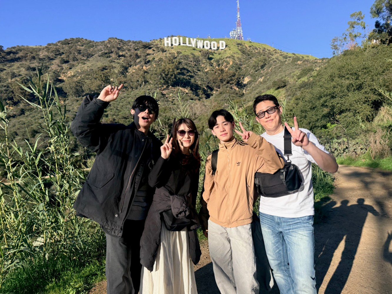 Group of tourists from Japan giving peace signs on the Hollywood Sign hiking trail with the full sign visible on the hillside behind them